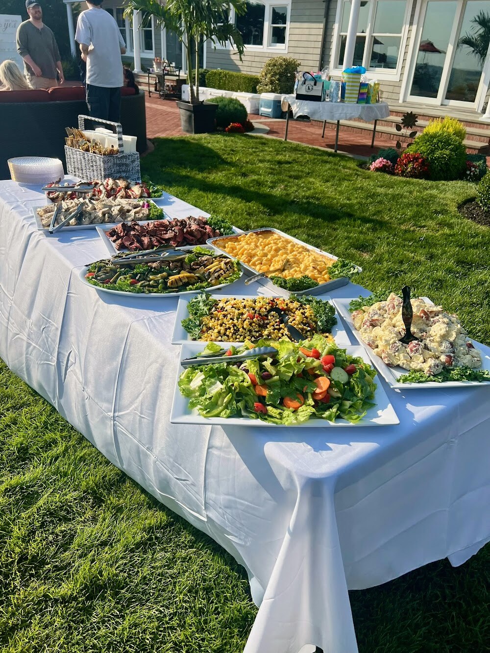 A long white-linen buffet table set on the lawn at a catered backyard event