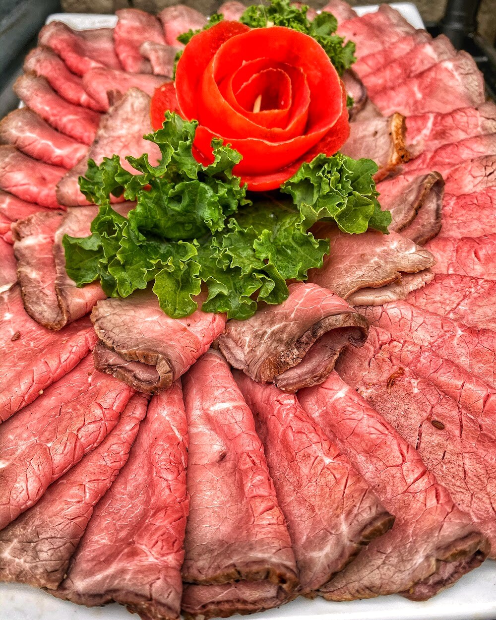 A cold-cut platter arranged with a tomato rose