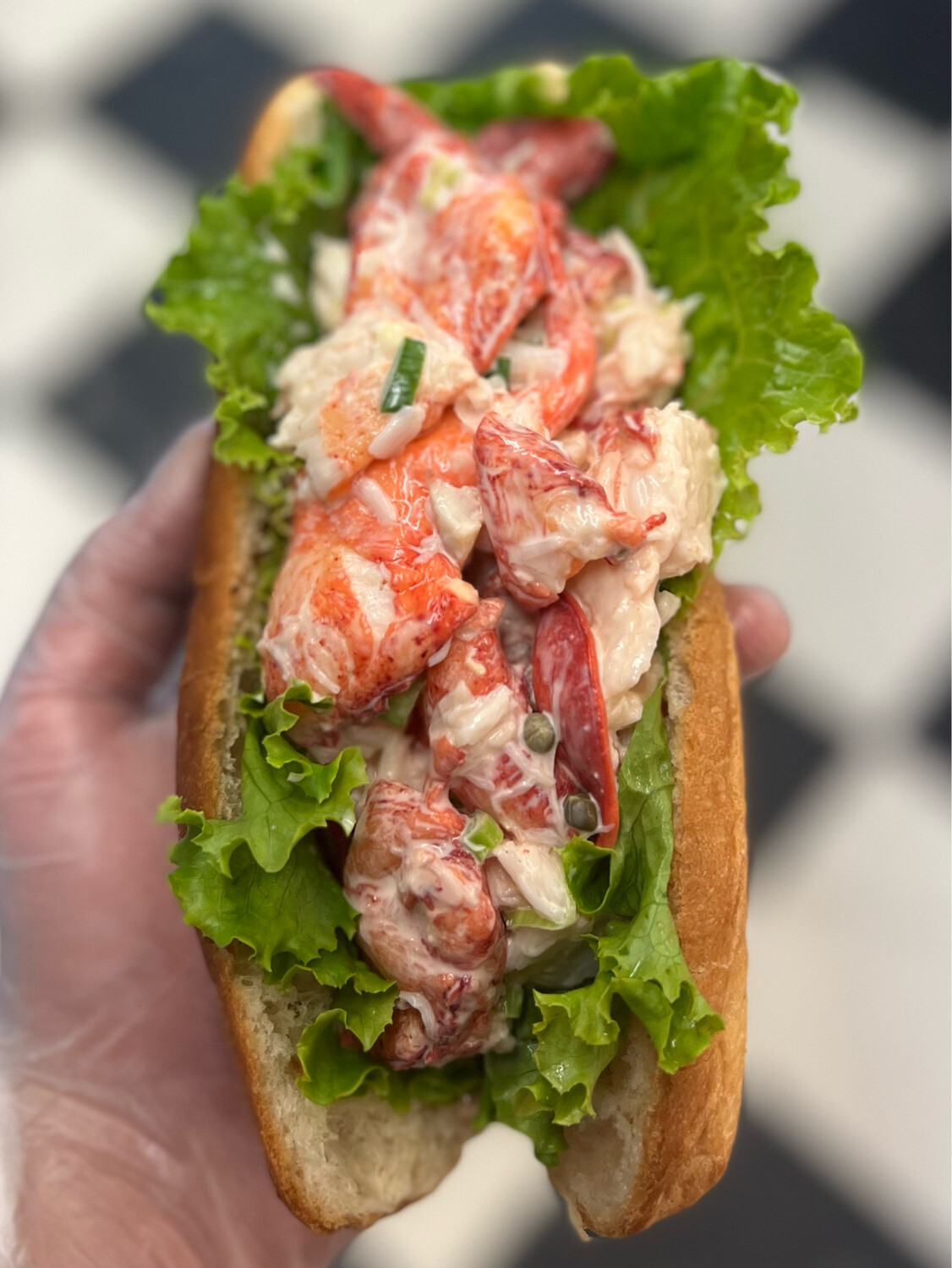 A lobster roll loaded over a split toasted bun, held at the counter